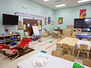 Colorful daycare room featuring tvs, tables, and activities